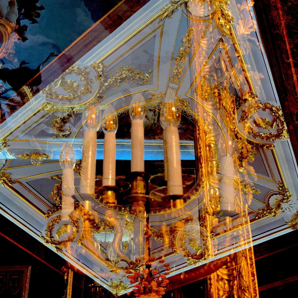 A golden chandelier layered with a painted ceiling.